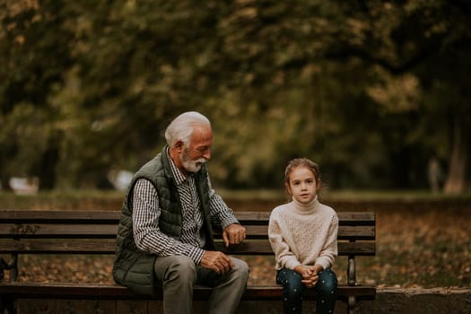 Handsome grandfather spending time with his granddaughter on bench in park on autumn day