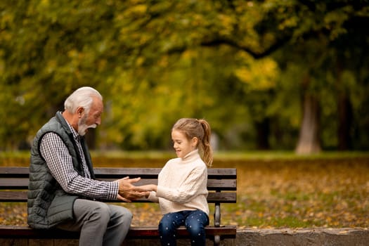 Handsome grandfather playing red hands slapping game with his granddaughter in park on autumn day