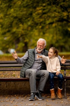 Handsome grandfather spending time with his granddaughter on bench in park on autumn day