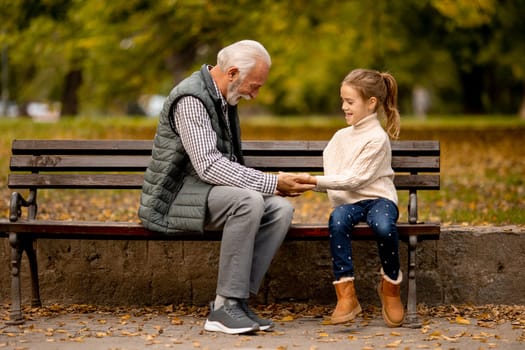 Handsome grandfather playing red hands slapping game with his granddaughter in park on autumn day