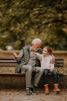 Handsome grandfather spending time with his granddaughter on bench in park on autumn day