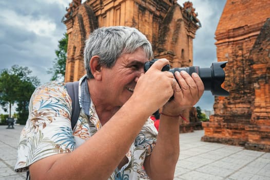 happy elderly man tourist traveling photographer with a camera takes pictures of landmarks at Po Nagar Cham Towers in Nha Trang in Vietnam in Asia