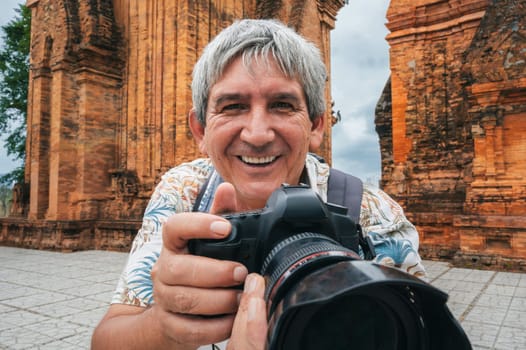 happy elderly man tourist traveling photographer with a camera takes pictures of landmarks at Po Nagar Cham Towers in Nha Trang in Vietnam in Asia