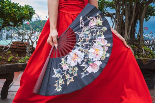 Beautiful Asian fan with flowers in female hand in red dress