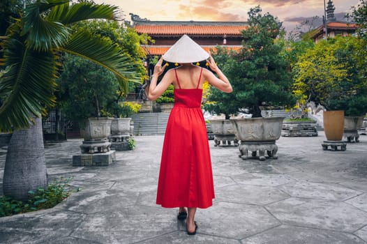 back of a female tourist traveler in a Vietnamese hat and red dress at the Long Son Buddhist Pagoda in Nha Trang in Vietnam. Travel and tourism in Asia