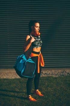 Young woman standing with sport bag outdoor after training