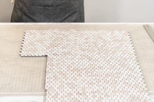 In the process of mounting peel and stick mosaic tiles onto a foam board, perfect for enhancing a food photography studio's aesthetic.