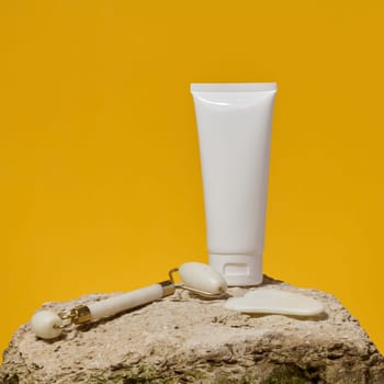 White tube, jade gouache massager and massage jade roller on a yellow background