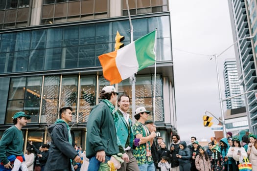 People are celebrating joyfully while waving an Irish flag during a lively city event