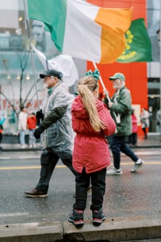 A girl joyfully watches a vibrant parade with the Irish flag displayed