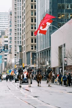 A lively parade with majestic horses and a large Canadian flag in the city