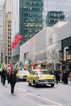Vibrant city parade showcasing diverse flags and a classic yellow taxi cab.
