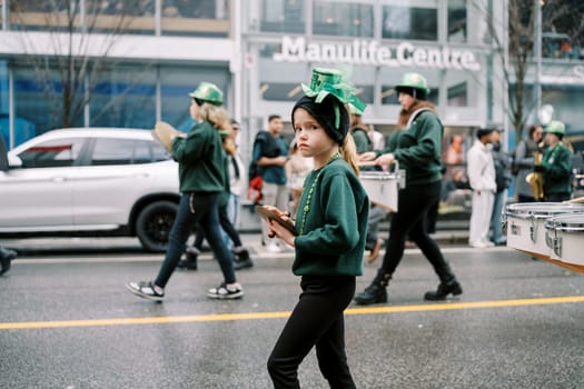 A group of young performers in green outfits joyfully join a lively parade