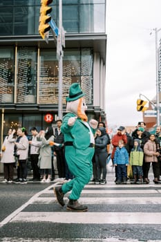 A lively leprechaun walks through a festive parade crowd on the street.