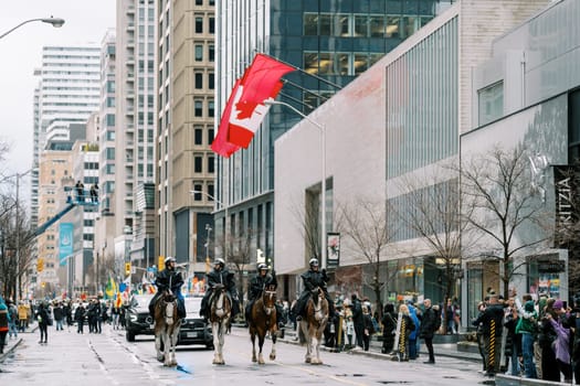 At a parade, mounted police display the Canadian flag amid excited crowds and decor