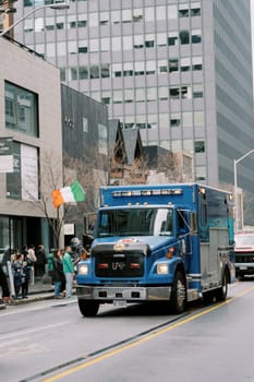 A blue ambulance rushes past crowds and tall buildings, creating urgency and excitement
