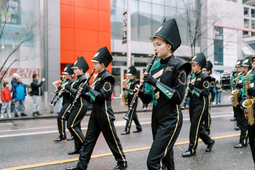 Young musicians in formal attire are joyfully playing instruments at a lively parade