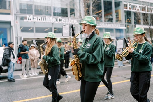 Marching band performing with saxophones and green hats in city parade