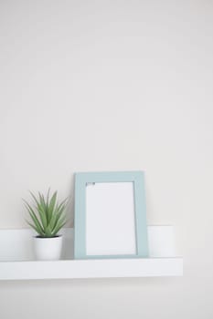 A minimalist shelf displays a plant and a blank picture frame, enhancing decor.