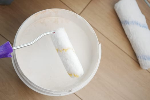 A roller brush rests in a bucket filled with paint as renovation begins.