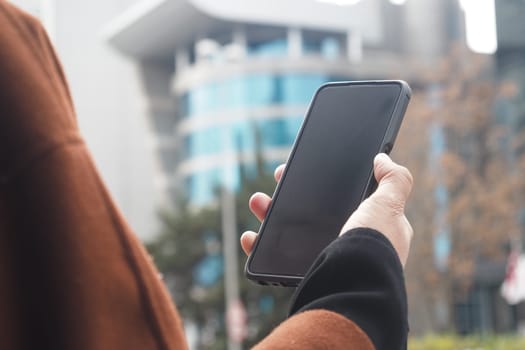 Individual displays a smartphone in a busy outdoor area with modern buildings.