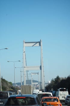 Vehicles travel along a highway under a clear blue sky with a bridge.