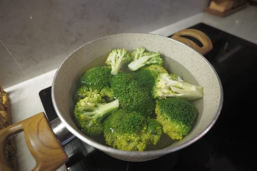 Fresh broccoli is boiling in a pot on the stovetop as dinner is prepared.