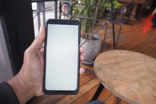 A person is holding a blank smartphone while seated at a table.