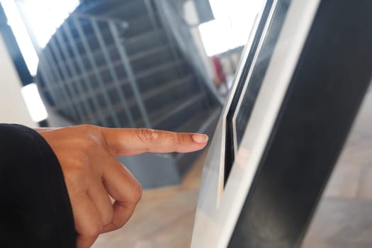 A hand touches a touchscreen interface in a contemporary building.