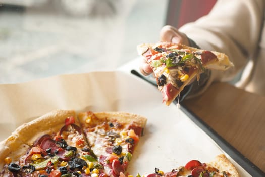 A person reaches for a cheesy slice of pizza topped with vegetables.