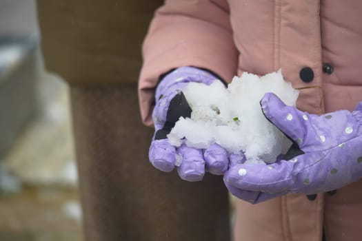 A child holds a handful of fresh snow, smiling with joy in the park.