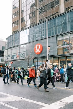 Groups of people casually walking past a Lululemon retail store on a busy urban street