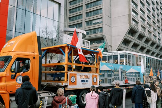 A vibrant parade with a decorated truck and a diverse crowd in the city