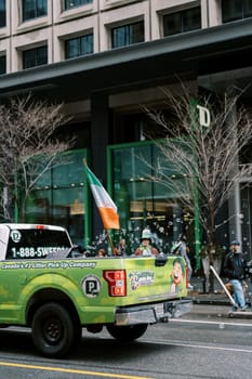 A parade features a pickup truck displaying an Irish flag, embracing the festive spirit