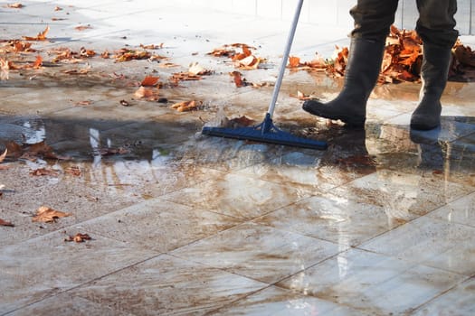 A person sweeps wet paving stones while cleaning fallen leaves.
