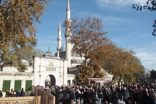 Crowds gather outside the mosque entrance on a sunny autumn day.
