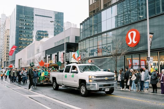 A vibrant and lively parade is passing various shops on a rainy day in the bustling city