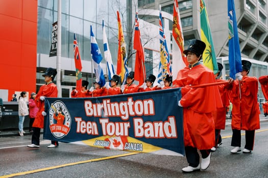The Burlington Teen Tour Band marches proudly with colorful flags in an energetic parade