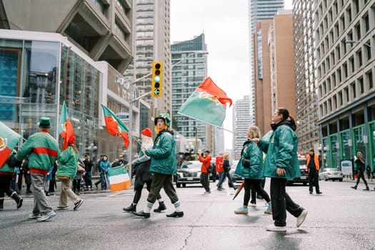 A group proudly holds colorful flags while marching through a bustling city parade