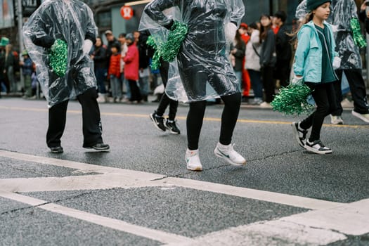 Participants in a parade wear rain gear and cheer for the excited onlookers