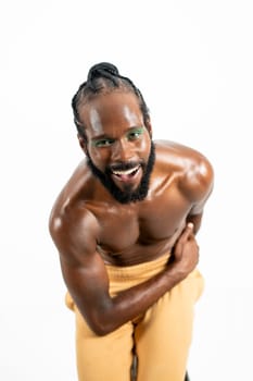 Happy African American shirtless gay model bending over white background. Portrait of cheerful homosexual man posing in plain studio