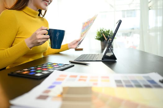 Creative designer holding a coffee cup working on color selection for a project at desk.