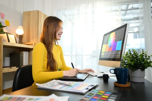 Smiling woman working on digital illustrations or design projects on her desktop computer.