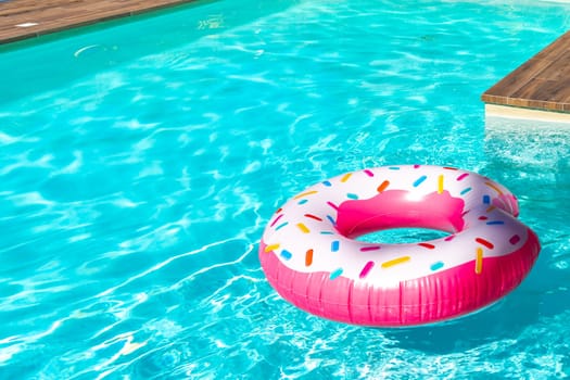 Pink donut-shaped inflatable float in turquoise swimming pool with wooden deck on a sunny day