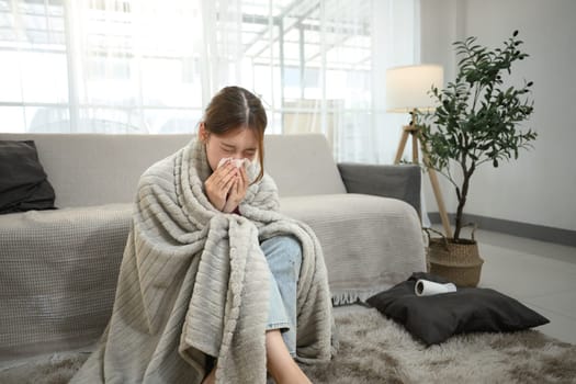 Unwell asian woman experiencing cold and flu symptoms, sneezing into a tissue.
