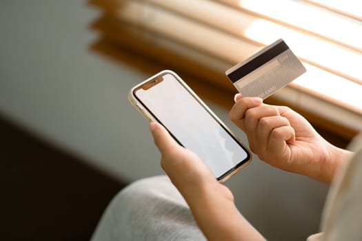 Hand holding smartphone with blank screen and credit card. Digital payments and financial security concept..
