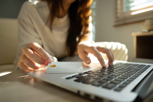 Close up of woman holding a credit card and typing on laptop, internet banking, or secure digital purchases..