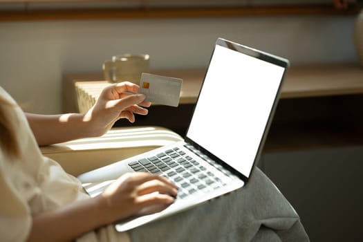 Close up of woman using a laptop while holding a credit card for online transactions.