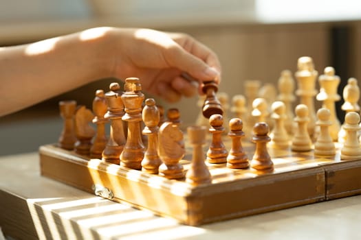 Hand holding chess piece, making a move on a classic wooden chessboard.