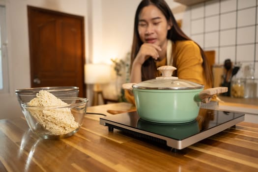 Happy asian woman in an apron stands in a kitchen, preparing a quick and easy meal.